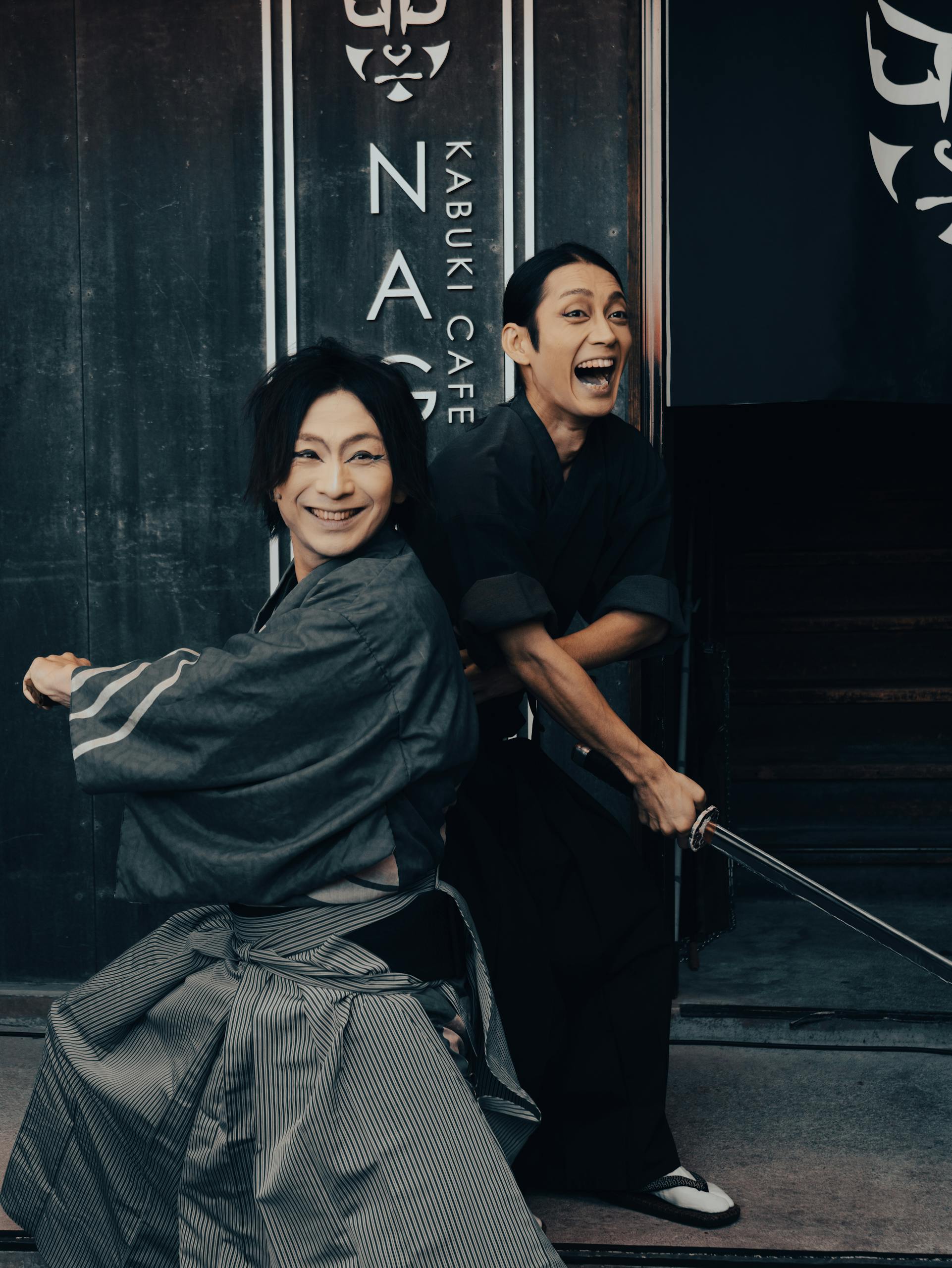 Two Kabuki actors smiling and posing with swords outside a Kabuki Café in Nagoya, Japan.